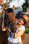 Woman in hat embrace brown horse