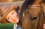 Woman in hat embrace brown horse. Close-up portrate