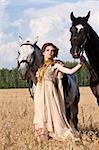 The woman in a beautiful old style dress with two horses in yellow field.