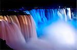 The American Falls of Niagara appear drenched in reddish and blueish lights on a beautiful evening.