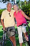 Happy senior man and woman couple together cycling on bicycles in a park