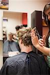 Portrait of a blond-haired man having a haircut with scissors