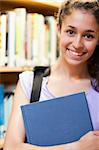 Portrait of a happy female student holding a book in a library