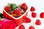 French creme brulee dessert with raspberries and mint covered with caramelized sugar in red heart shaped ramekin on white background