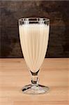A glassfull of fresh cold banana shake on a wooden table.