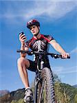 sports activity: young adult cyclist riding mountain bike and text messaging on cellphone. Vertical shape, low angle view