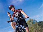 sports activity: young adult cyclist riding mountain bike and text messaging on cellphone. Horizontal shape, low angle view, copy space