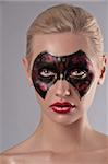 beauty face shot of a young woman having a black and red carnival mask painted on her face