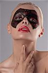 beauty portrait of a pretty blonde girl with a painted black and red carnival mask on her face and red lipstick