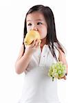 Little Asian girl eating pear and grapes, on white background