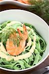 Green tagliatelle (ribbon noodle) with a cream sauce, shrimp and fresh dill served in a bowl (Selective Focus, Focus on the front of the shrimp)
