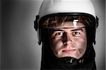 A picture of a young firefighter in a white helmet looking against grey background