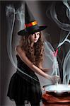 halloween shot of a young and beautiful witch wearing a huge black and orange hat making a poison in a big pot