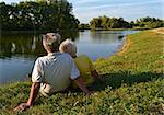 A senior couple sitting and relaxing together on a lakeside on a sunny afternoon.
