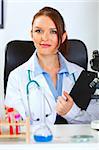 Female medical doctor sitting in cabinet with clipboard