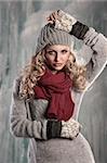 pretty young girl with curly blond hair in winter dress with hat and scarf playing and smiling to the camera