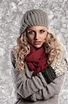 winter fashion shot of a beautiful girl with long curled blonde hair wearing a grey woolen cap, a grey sweater and warm gloves