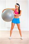 Full length portrait of smiling healthy girl holding fitness ball at living room