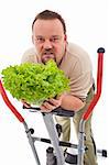 Chubby man on trainer device holding lettuce in sheer disgust