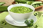 Fresh green pea soup with pea seeds and pea pods around (Selective Focus, Focus on the pea in the middle of the soup)