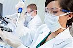 A Chinese Asian female medical or scientific researcher or doctor using a pipette and cell tray in a laboratory with her colleague out of focus behind her.