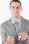 Portrait of a young businessman showing a miniature house and a set of keys with the camera focus on the objects