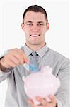 Portrait of a young businessman putting a twenty euros note in a piggy bank against a white background