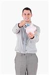 Portrait of a young businessman putting a note in a piggy bank against a white background