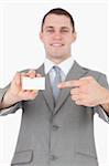 Portrait of a young businessman pointing at a blank business card against a white background