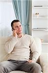 Portrait of a young man on the phone while sitting on his sofa in his living room