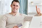 Smiling man shopping online with the thumb up in his living room