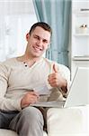 Portrait of a man shopping online with the thumb up in his living room