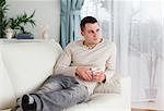 Pensive man holding a cup of coffee in his living room