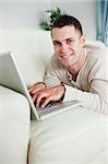 Portrait of a smiling man lying on a couch with a laptop in his living room