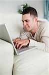 Portrait of a smiling man lying on a couch using a laptop in his living room