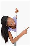 Smiling woman looking around the corner pointing at something on white background