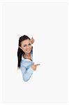 Smiling businesswoman looking around the corner while pointing against a white background