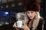 very attractive blond curly woman in elegant dress with fur stole and hat drinking a cup of tea