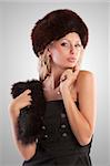 very beautiful fashion woman wearing an elegant black dress with boot and winter fur hat with stole on grey spotlight background