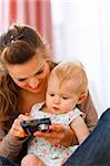 Young mother showing interested baby photos in camera at home