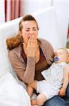 Young mother with sleeping baby on hands yawing at home