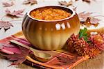 Pumpkin soup in ceramic pot, wooden spoon, flower and autumn leaf shallow DOF