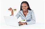 Businesswoman working with a notebook while eating a salad against a white background