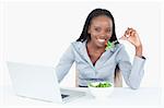 Cute businesswoman working with a notebook while eating a salad against a white background