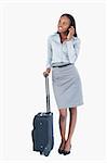 Portrait of a cute businesswoman with a suitcase making a phone call against a white background