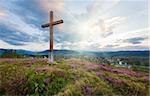 Summer evening country foothills view with heather flowers and wooden cross on sky with sunshine background (Lviv Oblast, Ukraine) .