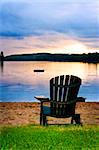 Wooden chair on beach of lake at sunset