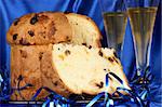 Panettone the italian Christmas fruit cake served on a blue glass plate and two glasses of Spumante over a blue fabric background. Selective focus.