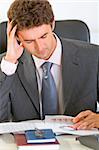 Stressed modern businessman sitting at office desk and working with documents