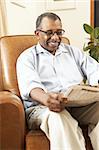 Senior Man Sitting In Armchair Reading Newspaper